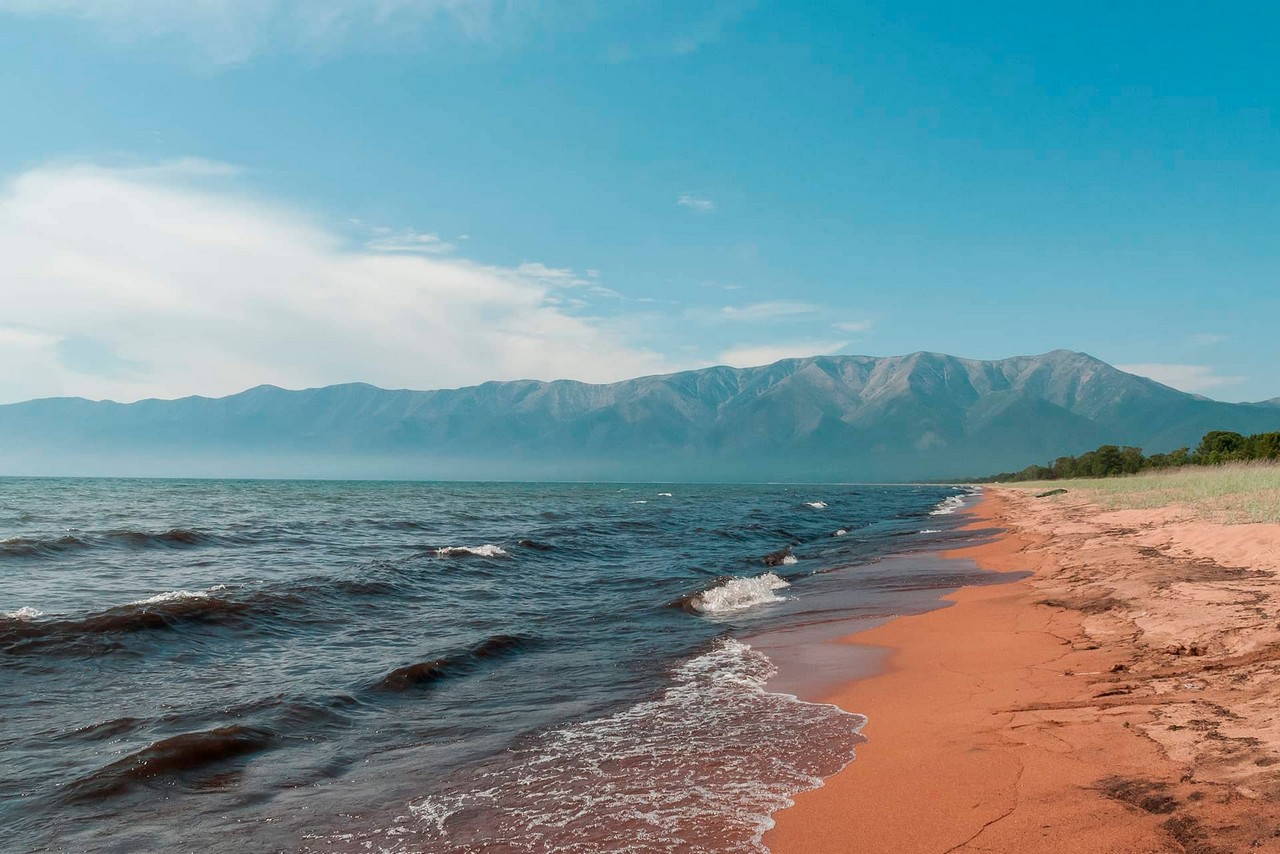 Sandy shore of lake Baikal and mountains behind it