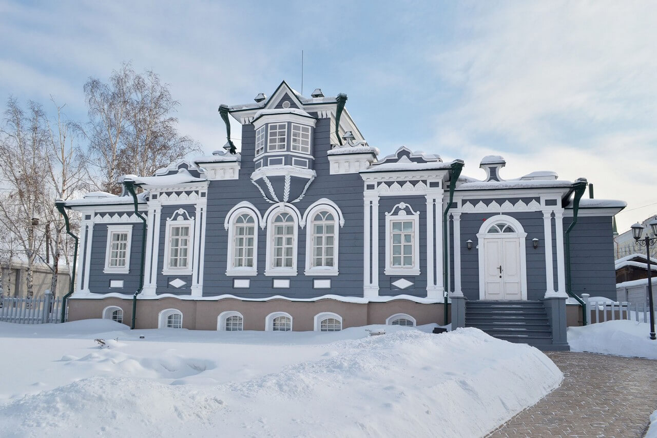 A grey and white wooden house built in the style of classical noble mansions decorated with a bay-window in winter