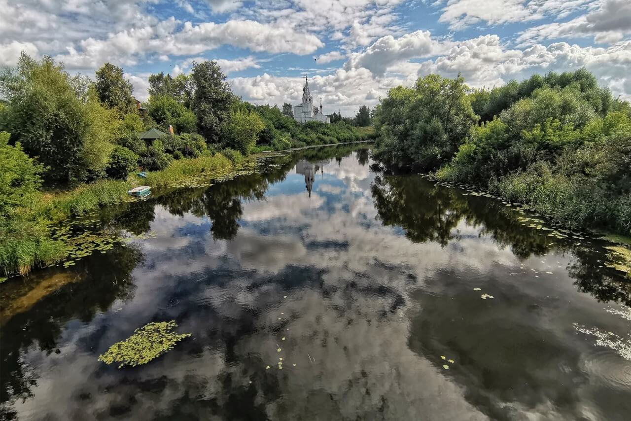 A small river and white church in the background with its reflection in the water in summer.