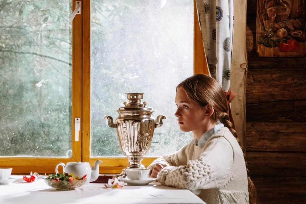 A Russian girl in front of a table with samovar, tea cups, teapot and sweets