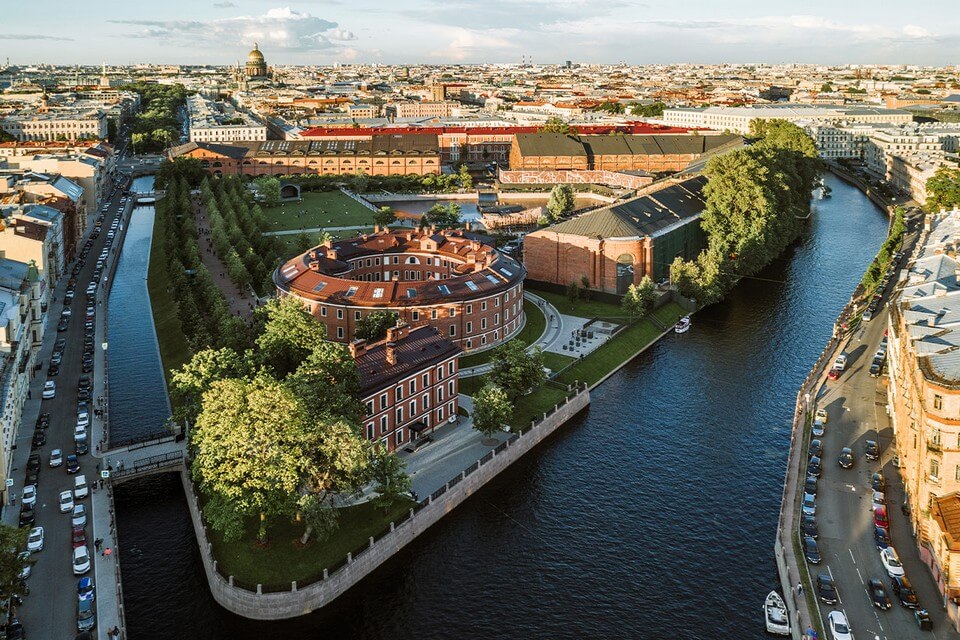 Aerial view of a park located on an island, round brick building in front, view over Saint-Petersburg in the background