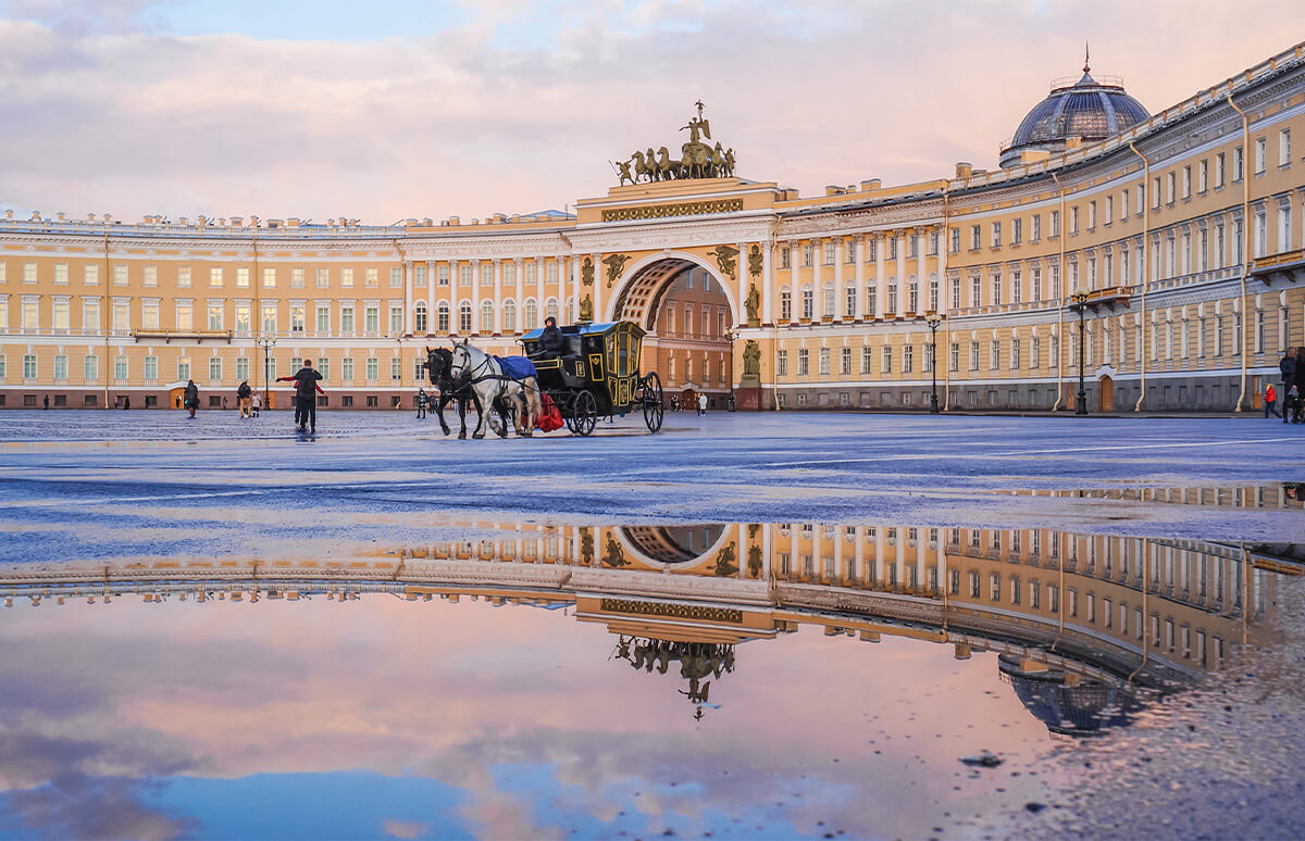 Yellow and white building with a 580 m long bow-shaped facade. It consists of two wings, which are separated by a tripartite triumphal arch adorned by sculpture, monumental Neoclassical building in the Empire style. Vintage horse carriage in front of the palace. Reflection of the palace in a puddle of water.