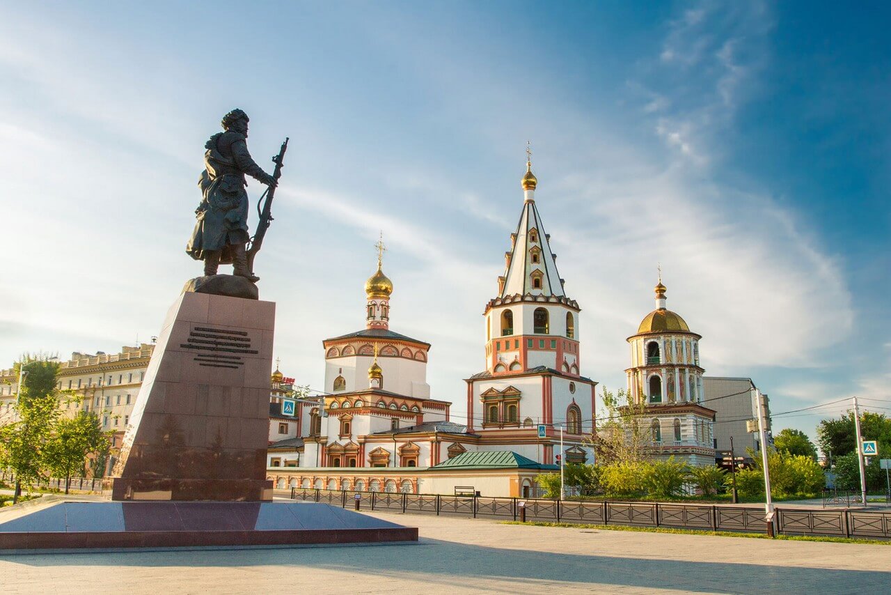 A colorful ornate orthodox church in baroque style, A bronze monument of a man on a granite base in front of the church