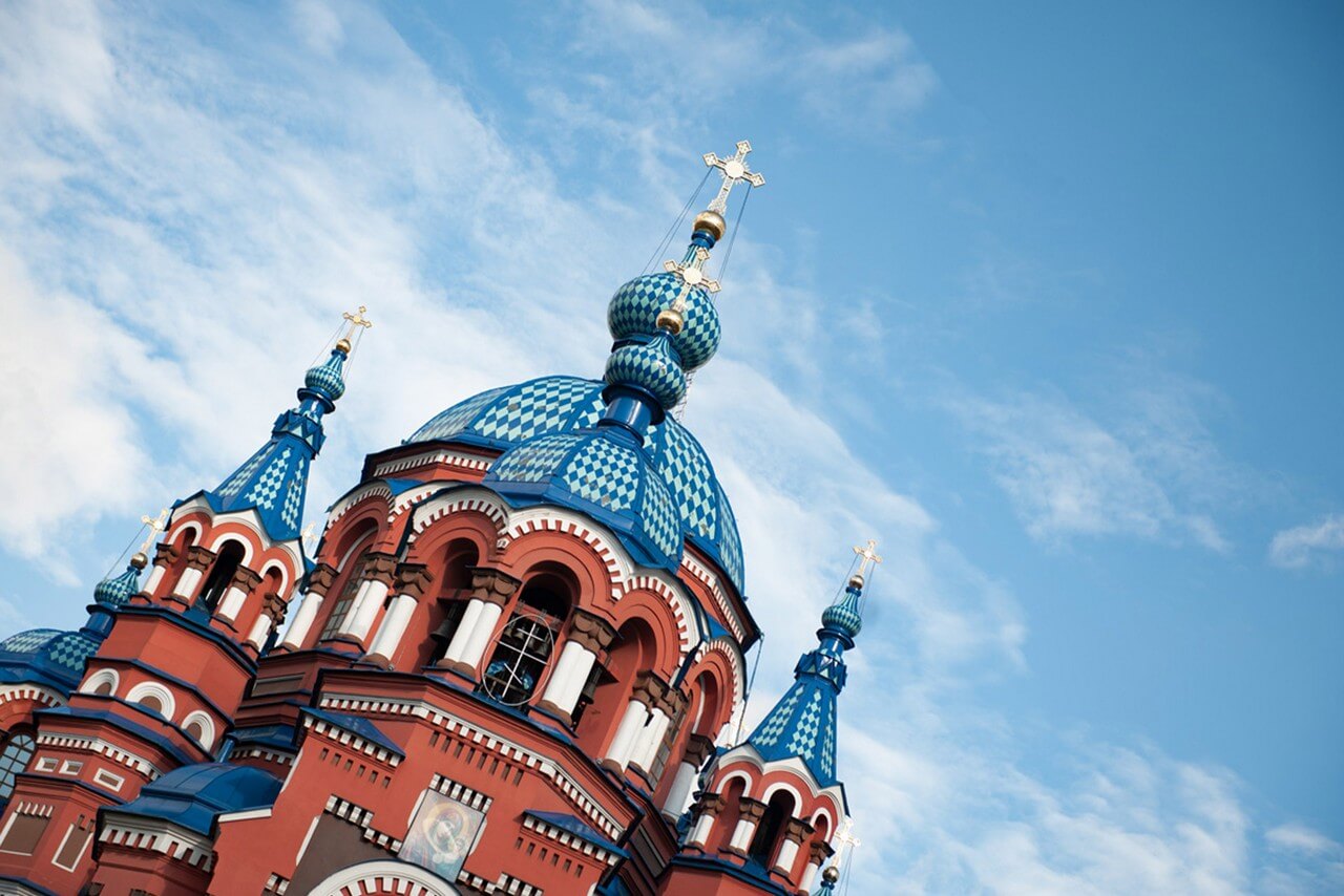 The top of a red church, blue domes of an orthodox church with a gilded cross against the blue sky, the icon of Madonna with a child.