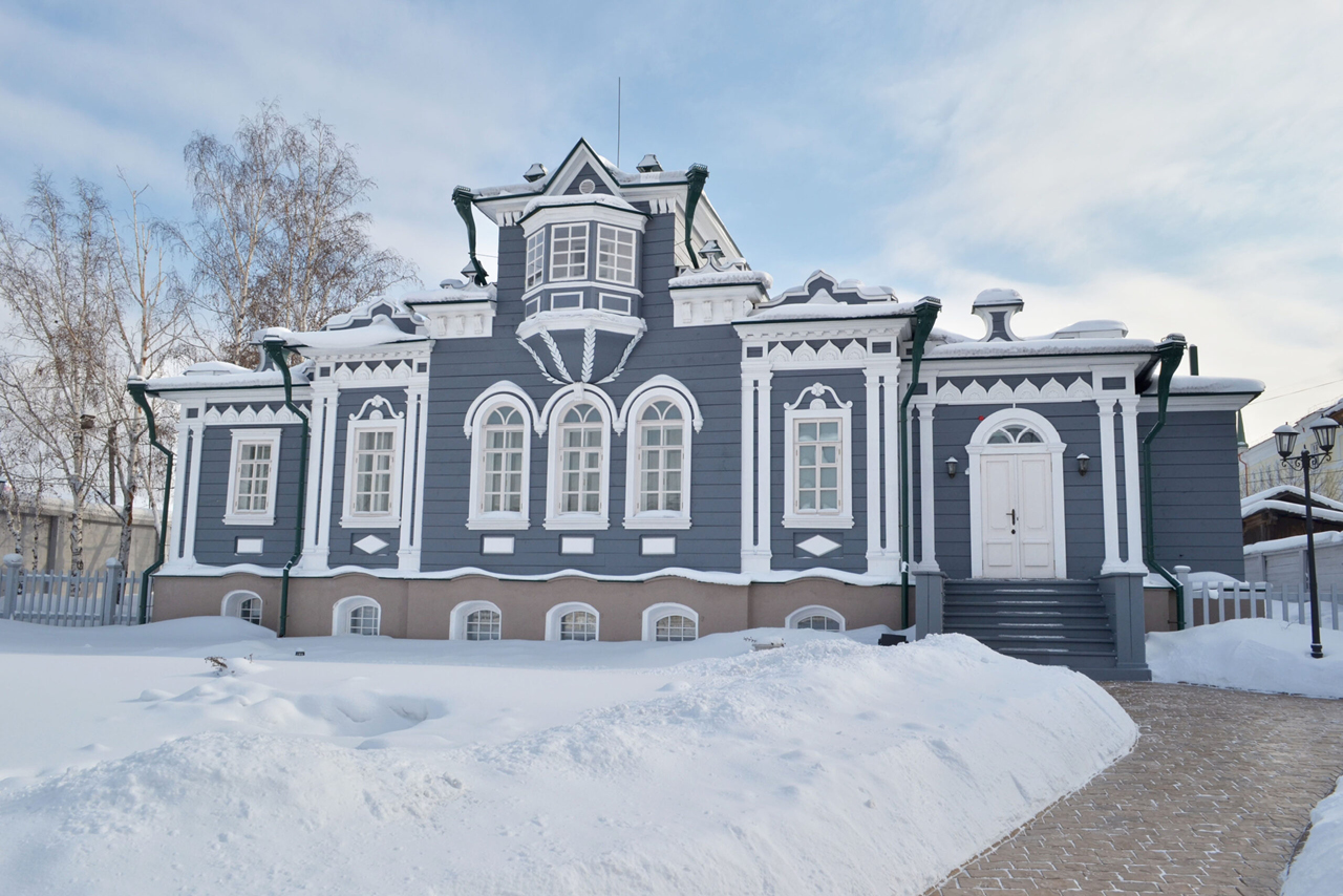 A grey and white wooden house built in the style of classical noble mansions decorated with a bay-window in winter