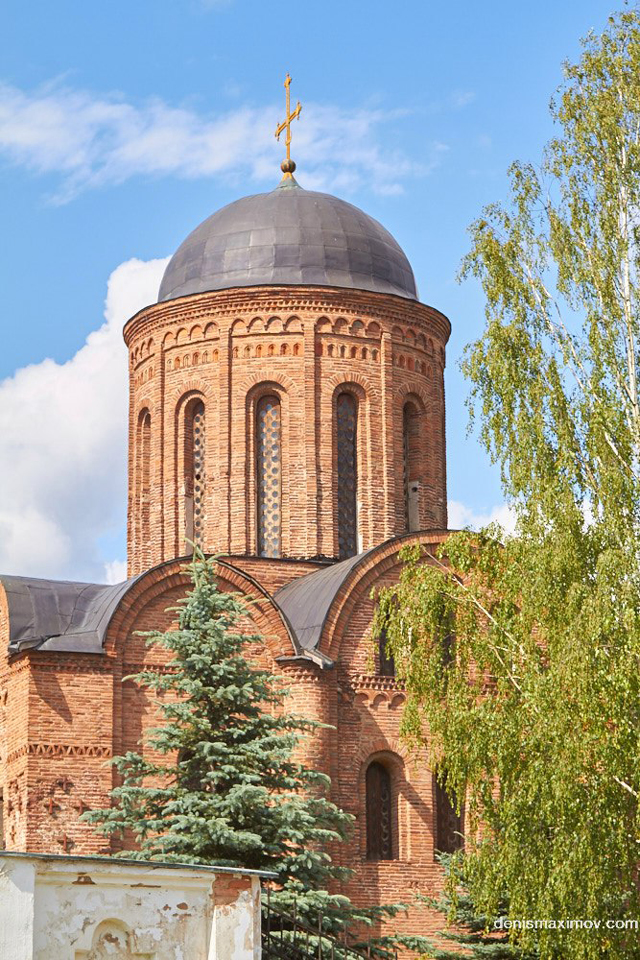 A round main tower of a red brick orthodox church with many narrow arched windows around it and a massive metal cupola on the top