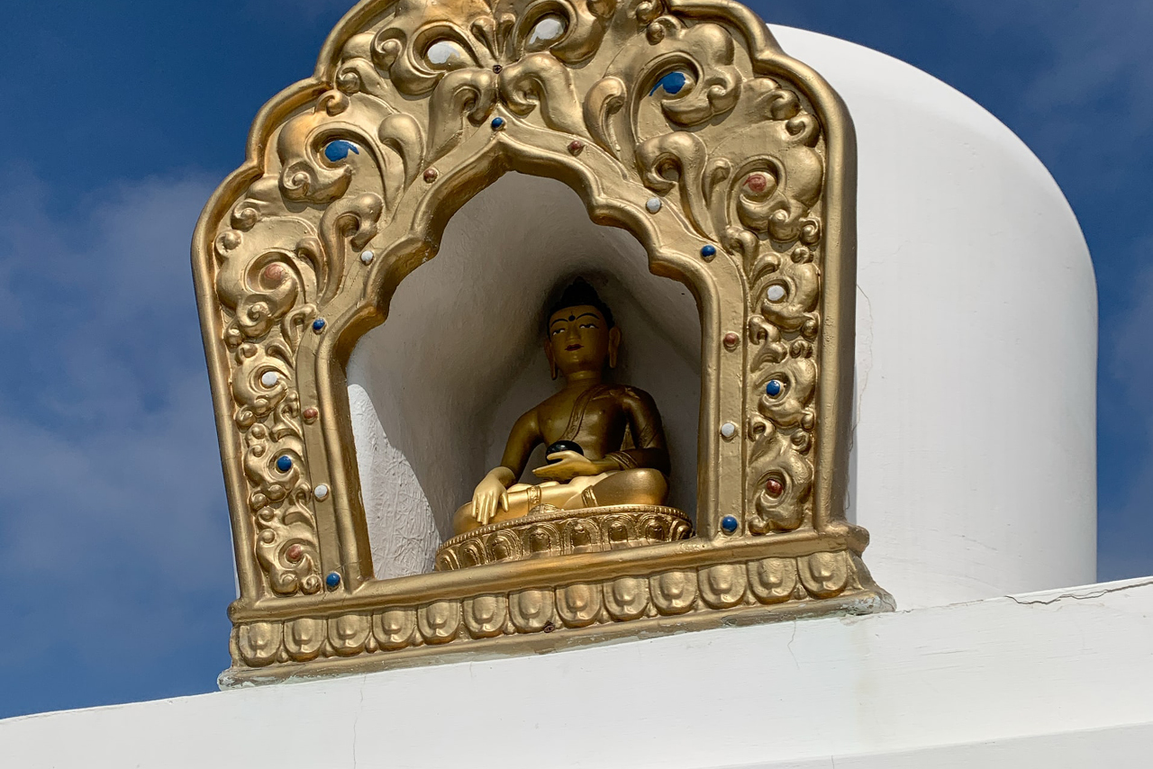 Golden Buddha sitting in an decorative arch as an element of a Buddhist stupa