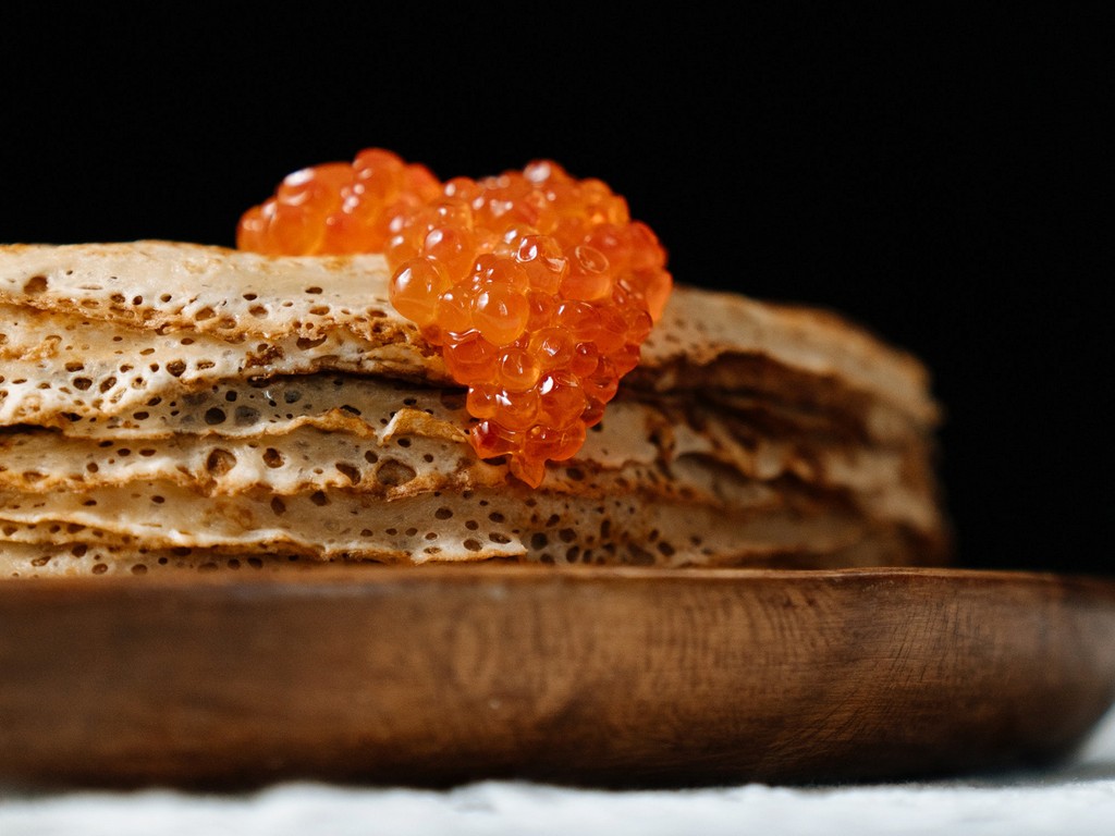A pile of pancakes decorated with red caviar on the top, served on a wooden plate, Russian restaurant, local food