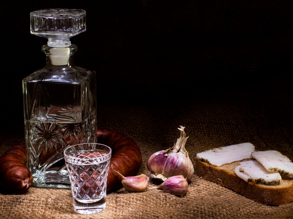 A beautiful crystal glass bottle and a glass with vodka served with garlic, sandwich with salo, salami, vodka degustation