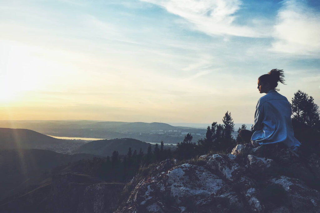 A girl sitting on the top of a mountain watching the river and beautiful landscape