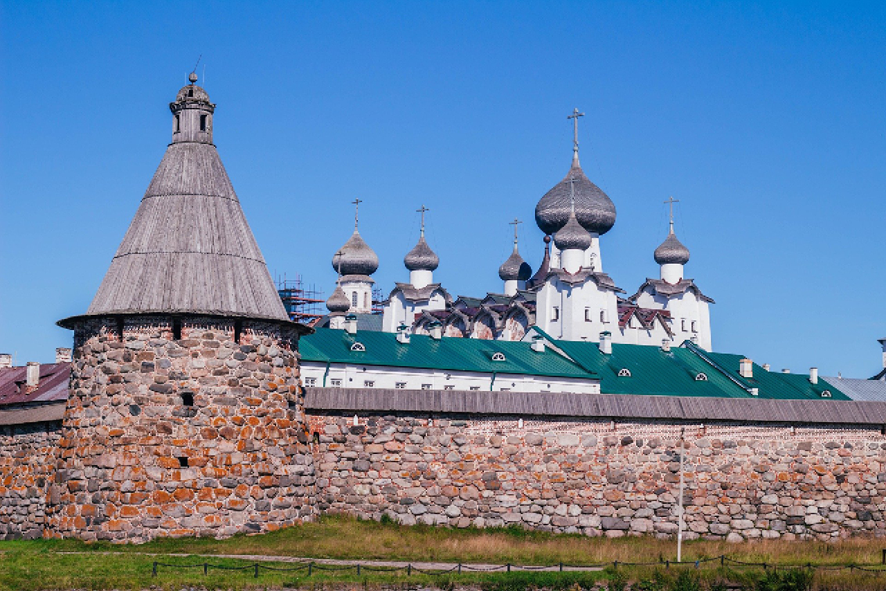 A fortified wall with a tower made of stone and onion domes of a cathedral behind the wall on the territory of the monastery
