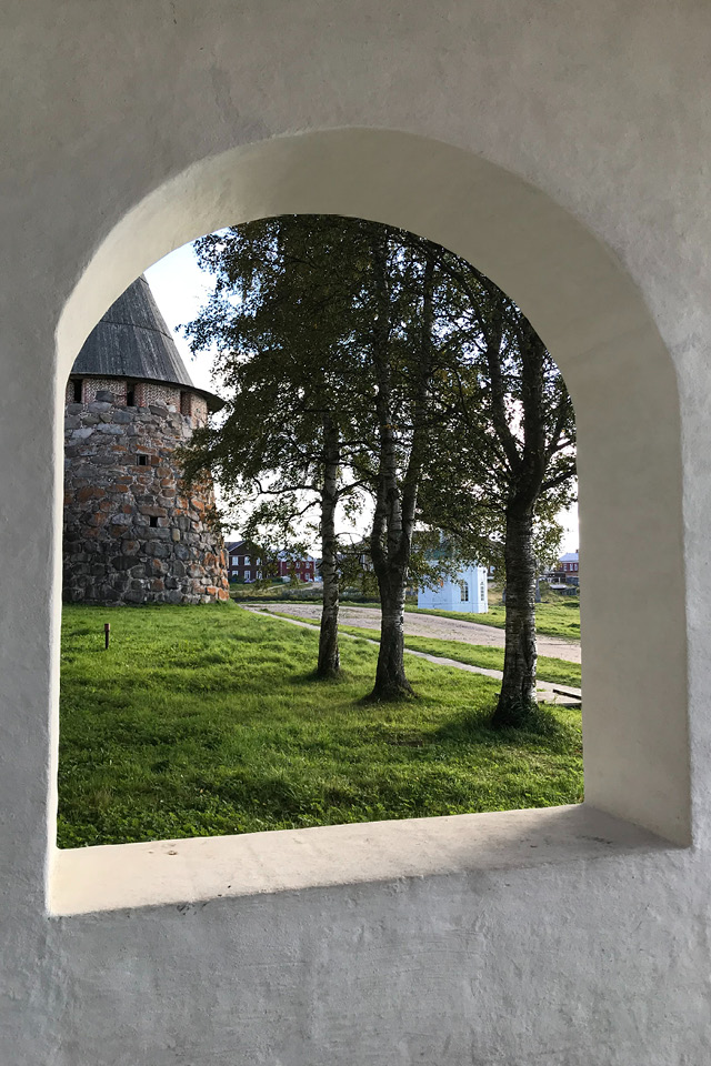 A view from an arched window of a fortress to the street, trees and a round stone tower