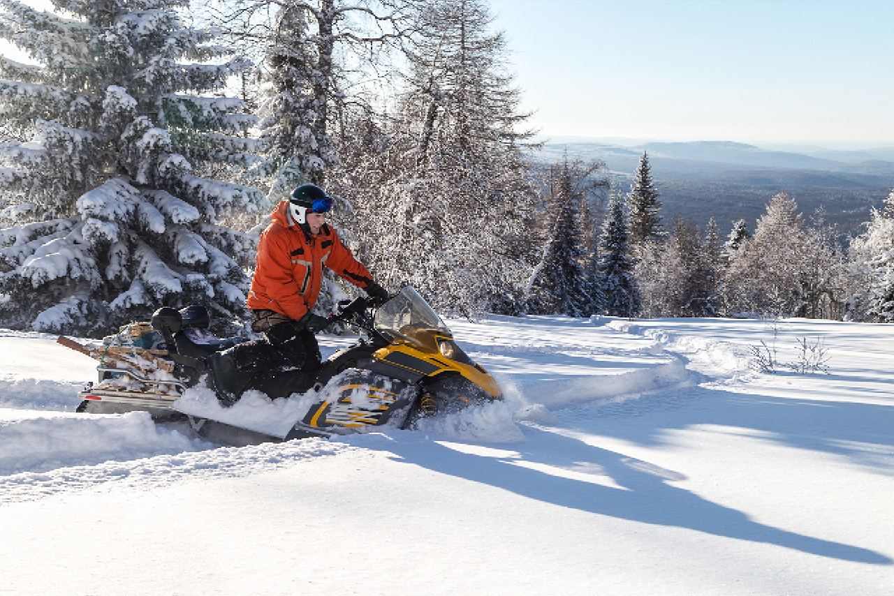 Woman in red jacket riding a snowmobile in the winter forest