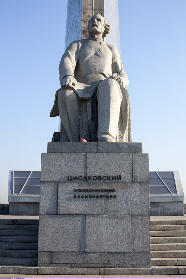 A monument of a man of the 20th century with long hair and a beard sitting, a quadrate base of a monument with a sign in Cyrillic