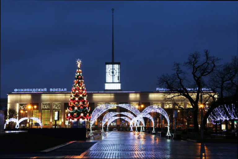 A railway station building in modern style with a glass clock tower with a spire, a Christmas tree and decorative lights