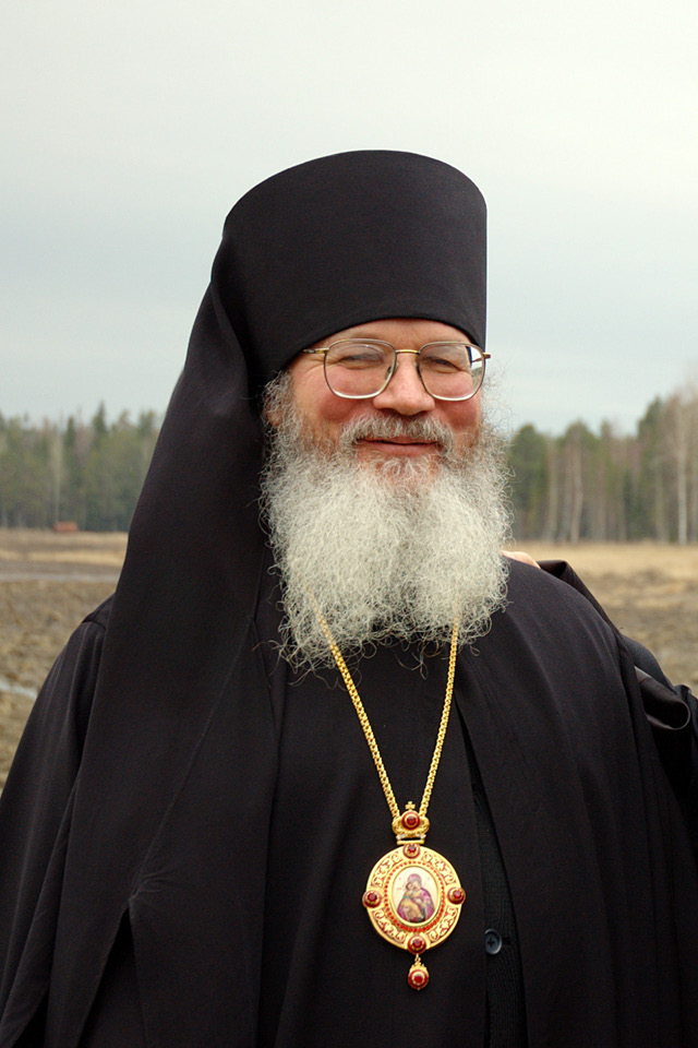 A happy monk with white beard wearing black clothes and a golden medallion