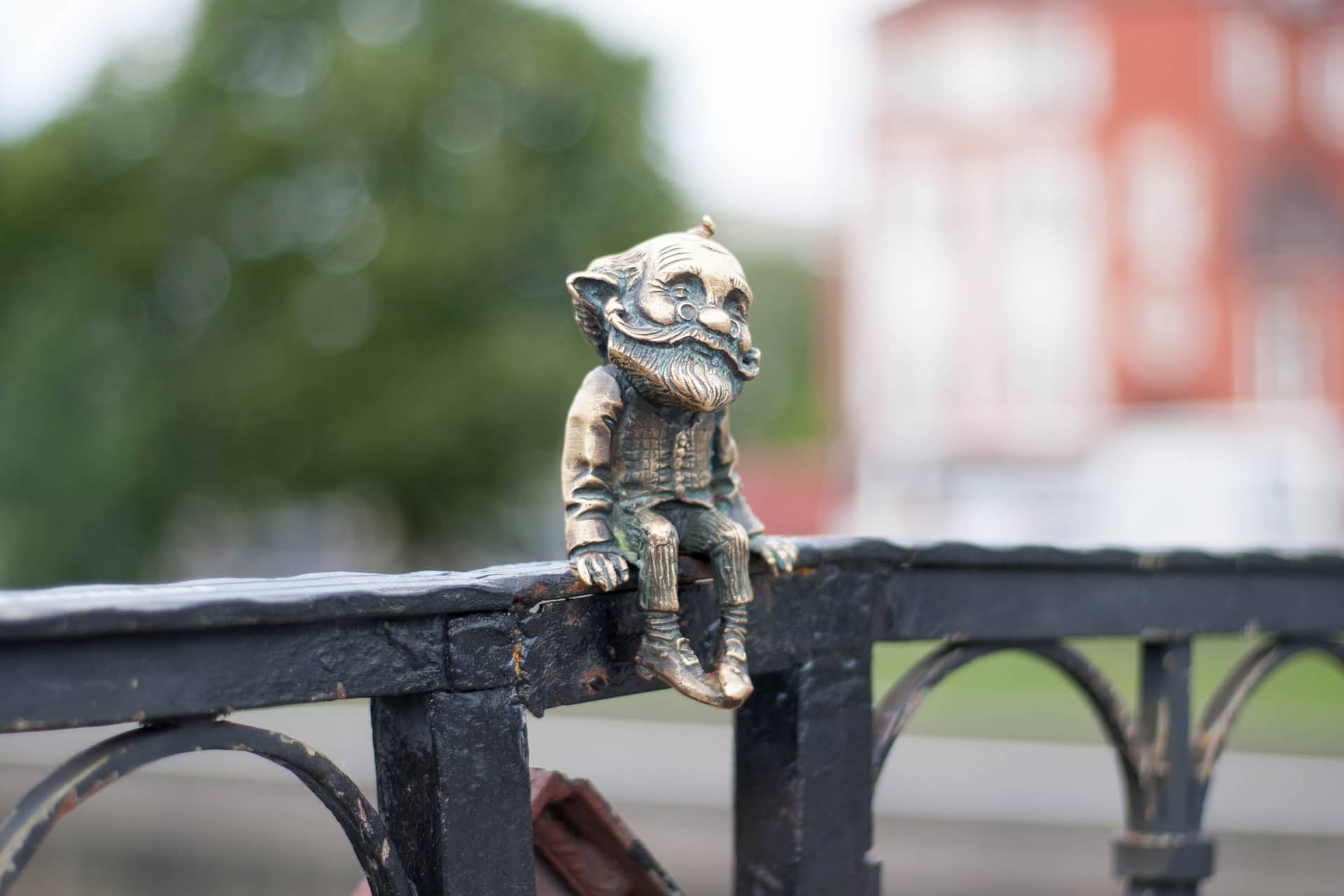 A small bronze statue of an old man sitting on a bridge fence