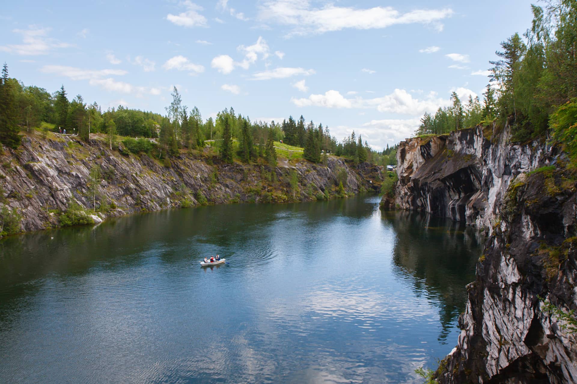 A marble quarry surrounded with marble cliffs with pine forest on the top, a boat on the water