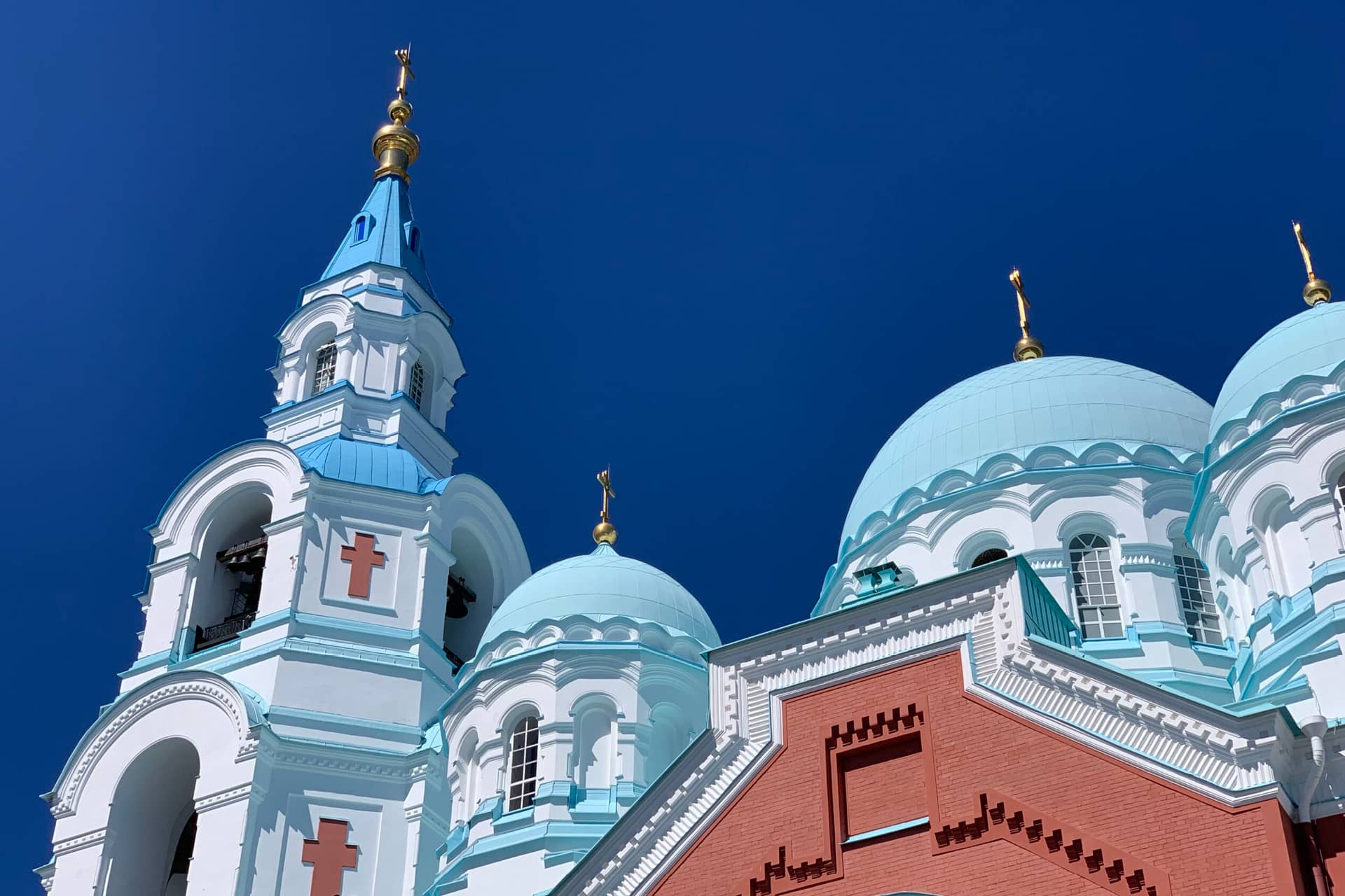 View of the top of Orthodox cathedral from the ground. Orthodox cathedral with the red base, white towers and blue domes topped with gilded crosses, bell tower decorated with red orthodox crossed