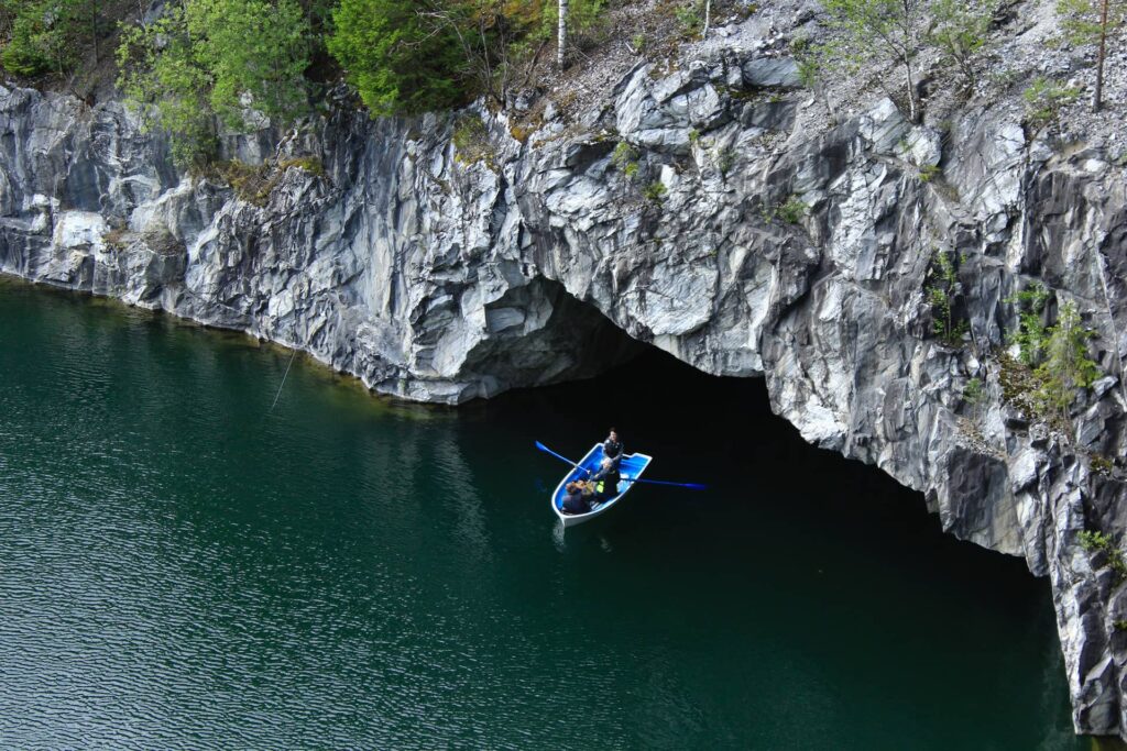 A small boat and people with peddles on the water of the marble quarry surrounded with marble cliffs, a natural cave in the marble rock
