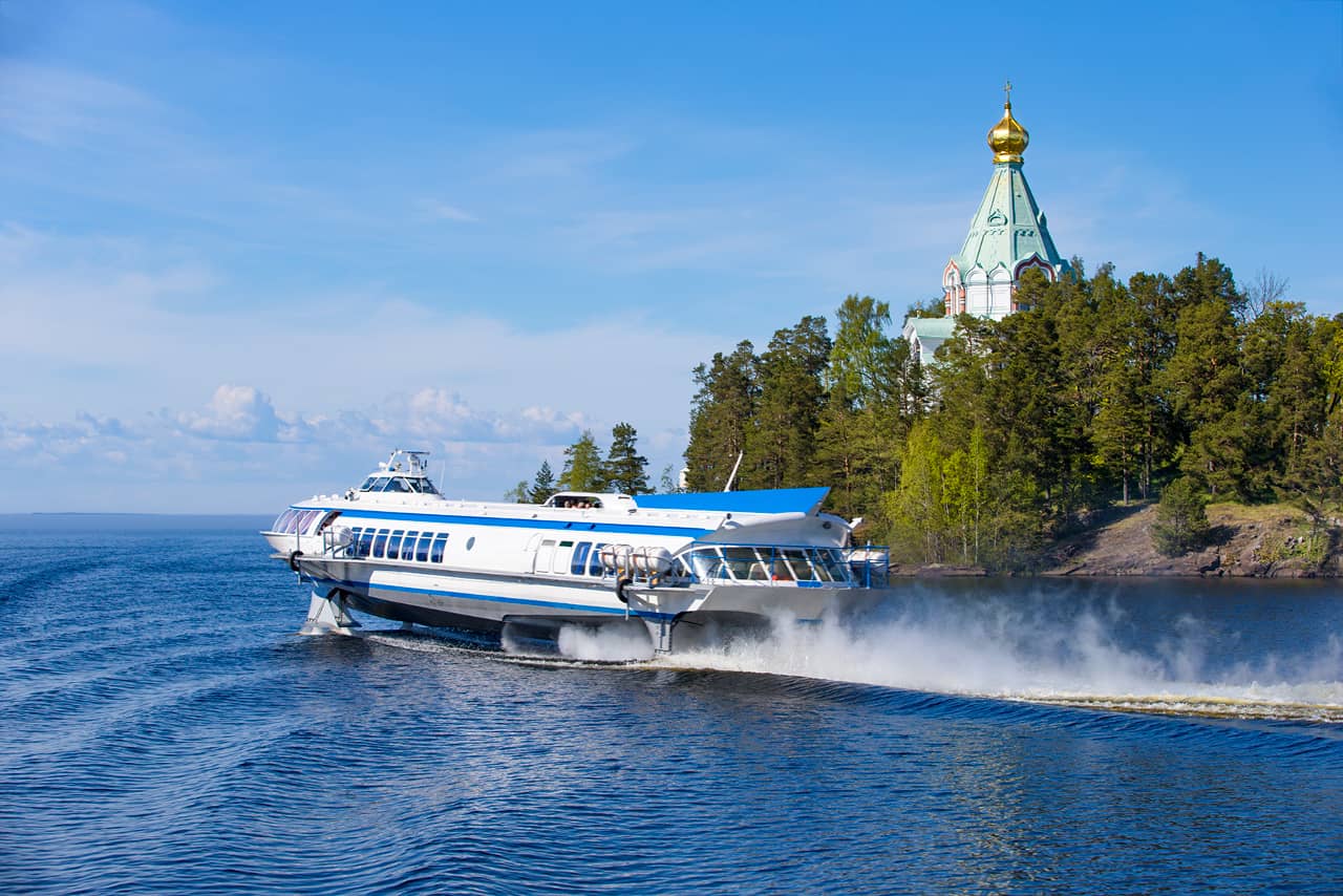 A hydrofoil passenger boat on the lake, island with cliffs, green trees and a church on it, northern nature.