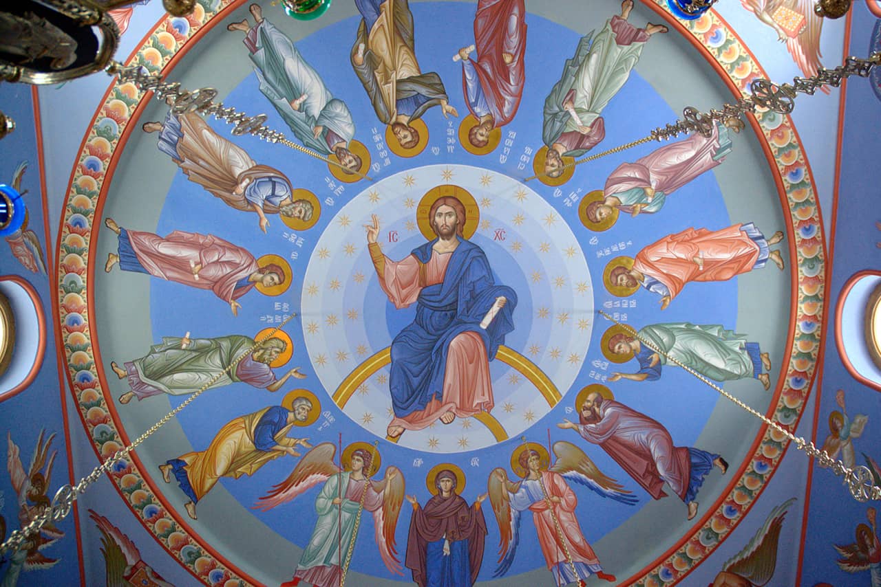 A round fresco in a church with a Jesus Christ in the center and saints around him against the blue sky