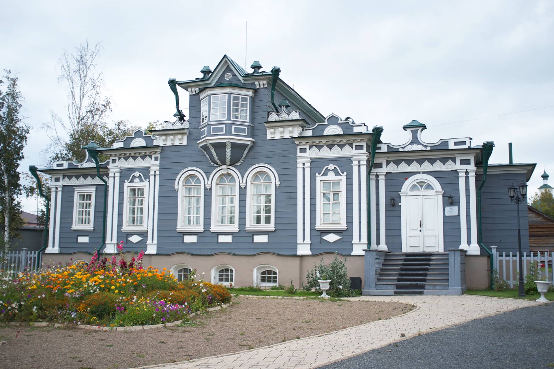 A grey and white wooden house built in the style of classical noble mansions decorated with a bay-window