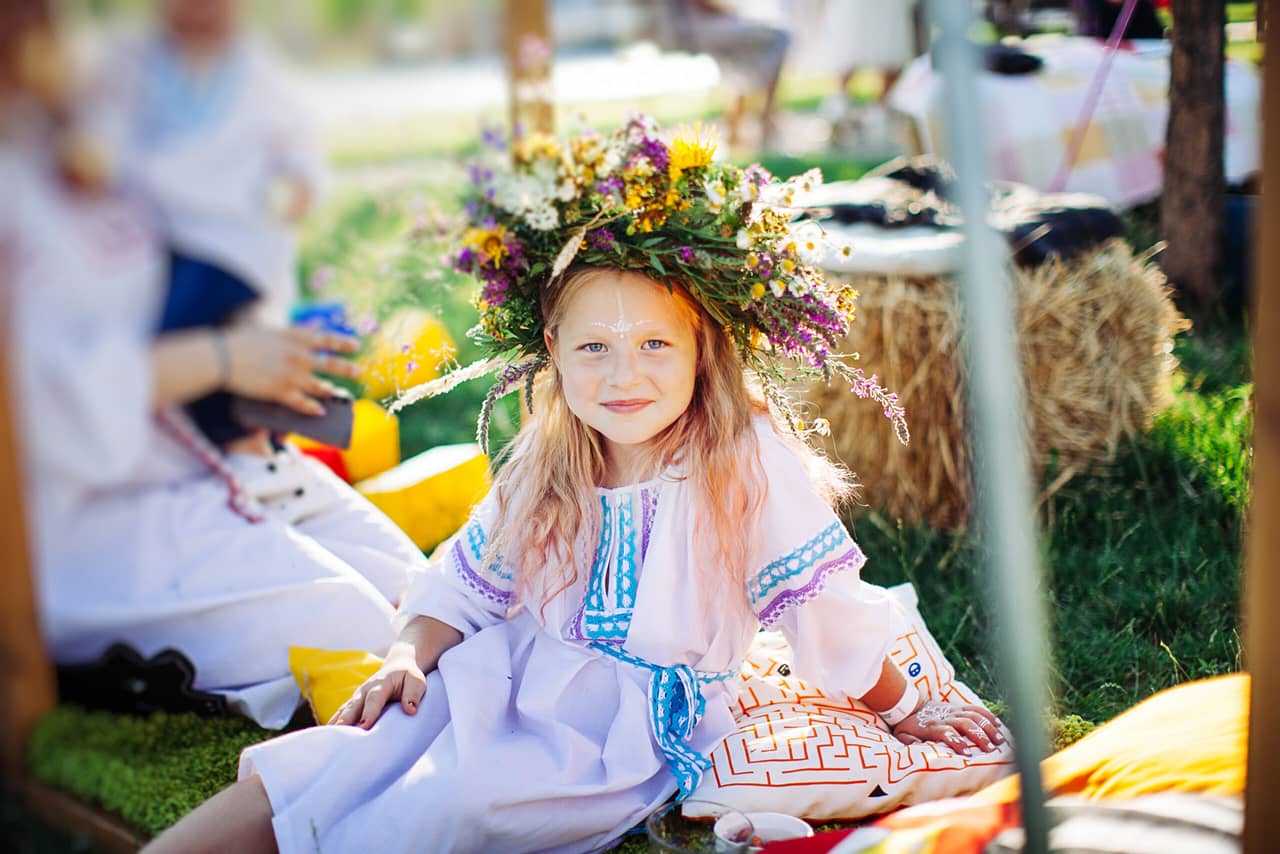A young girl wearing traditional Russian clothes with a flower crown smiling