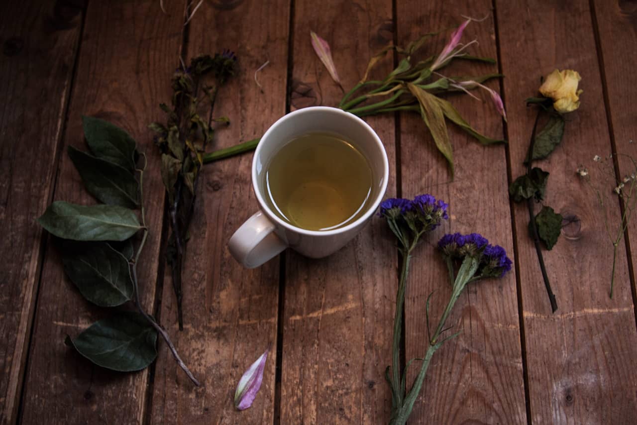 A cup of tea on a wooden table, flowers and herbs around it