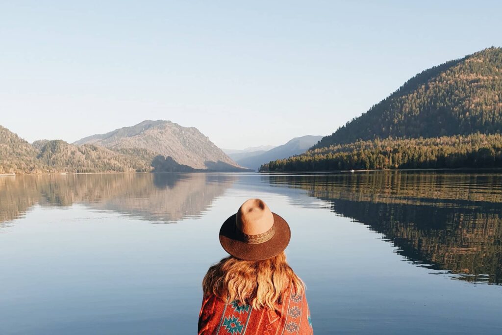 A young woman wearing a hat in front of a lake and mountains