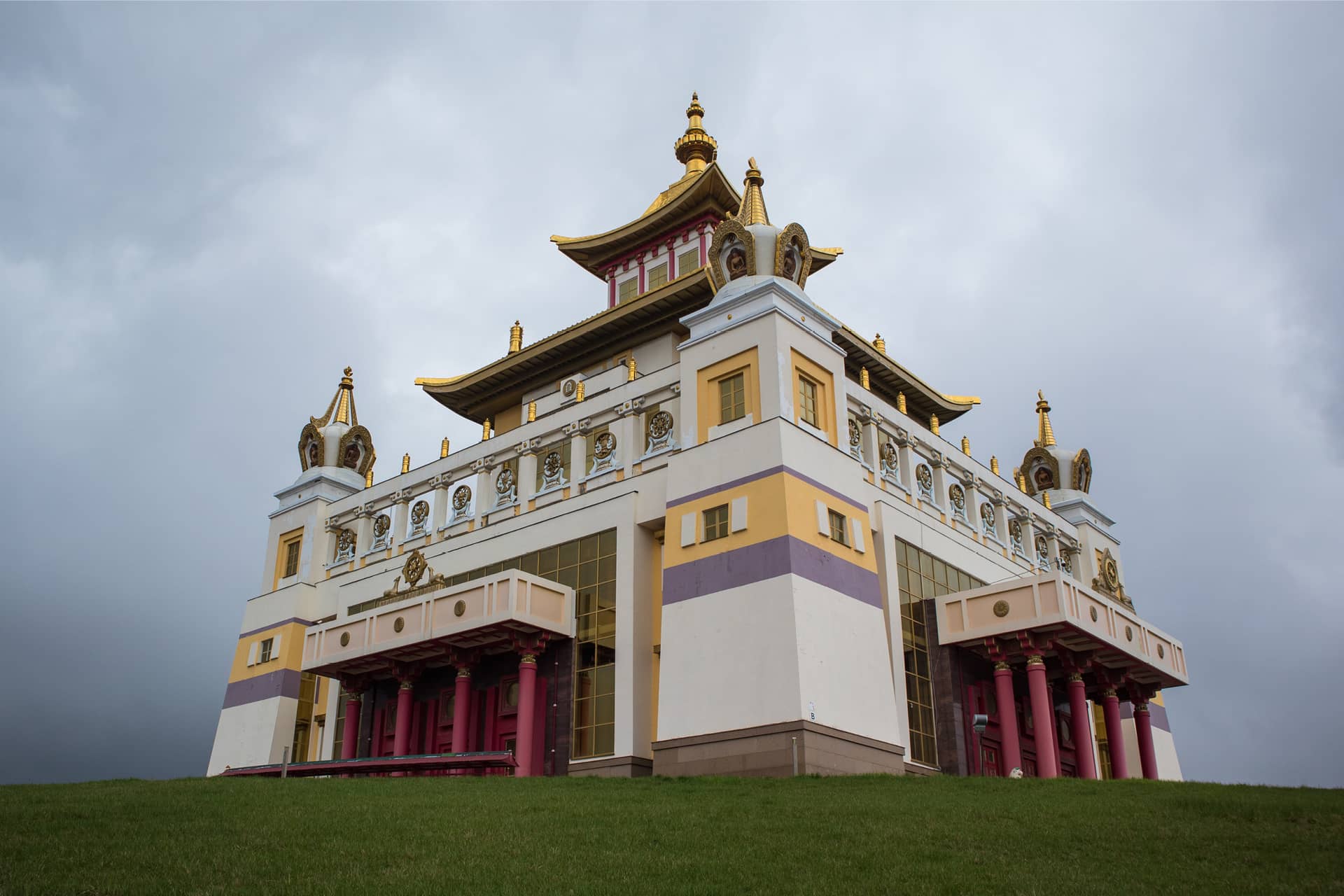 A massive white and golden Buddhist temple with red gates on a hill