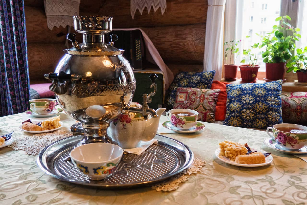 A shiny samovar and porcelain cups on a table, tea served in a Russian family, room in a wooden house