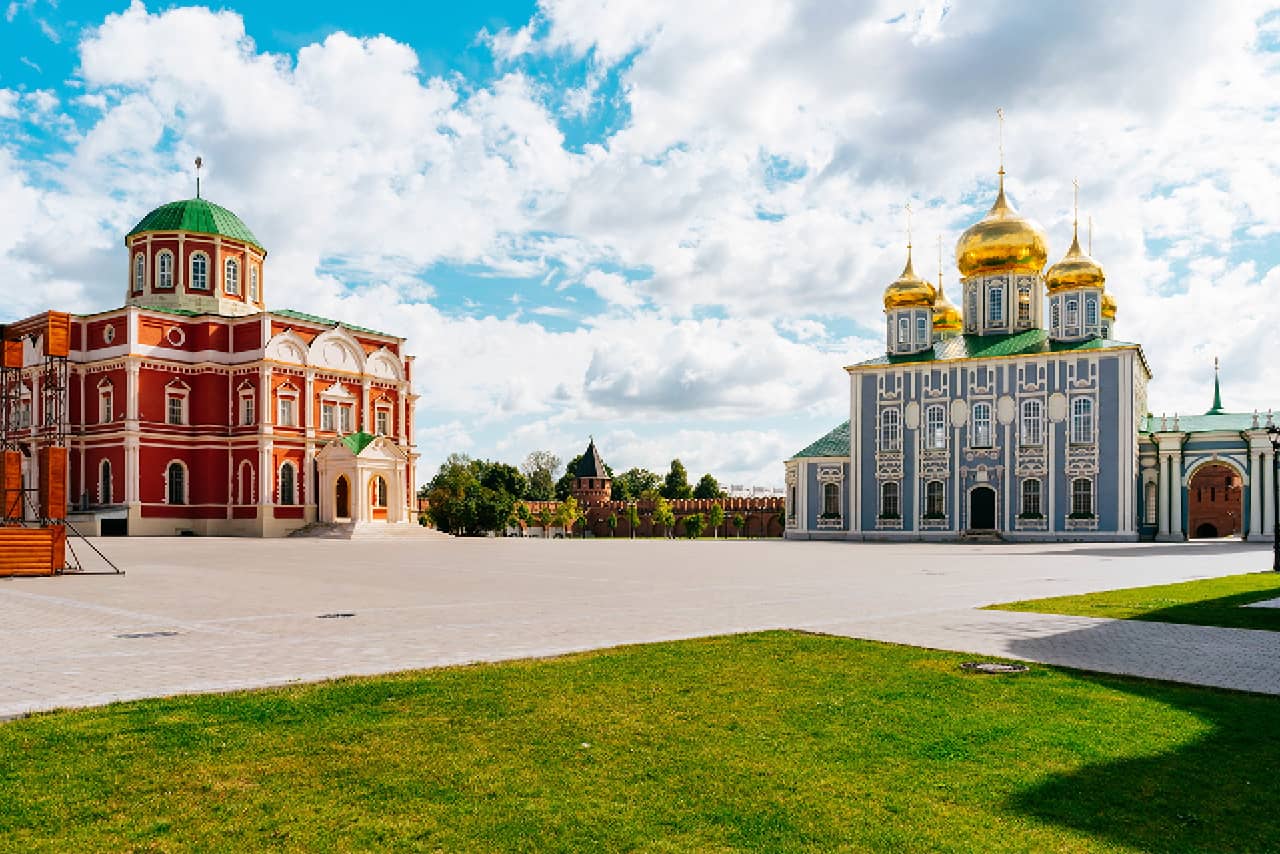 A red and white cathedral with round green dome on the left and grey and white tall cathedral with five onion gilded domes