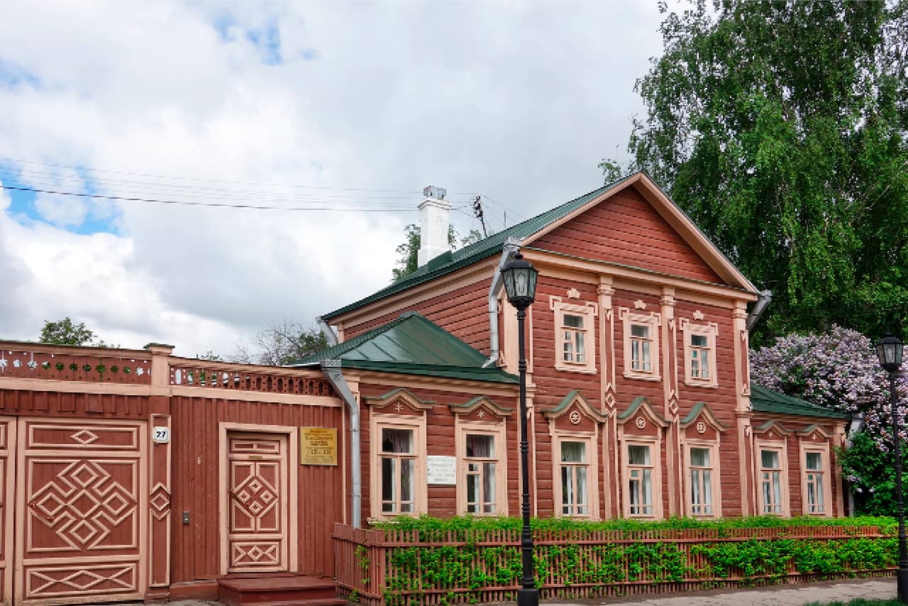 A red wooden house with green modern metal roof and decorations around windows. A memorial plate and a number of house 77 on the facade of the house, Museum at the estate of Nobel Prize winner IP Pavlov with furnished rooms & science exhibits.