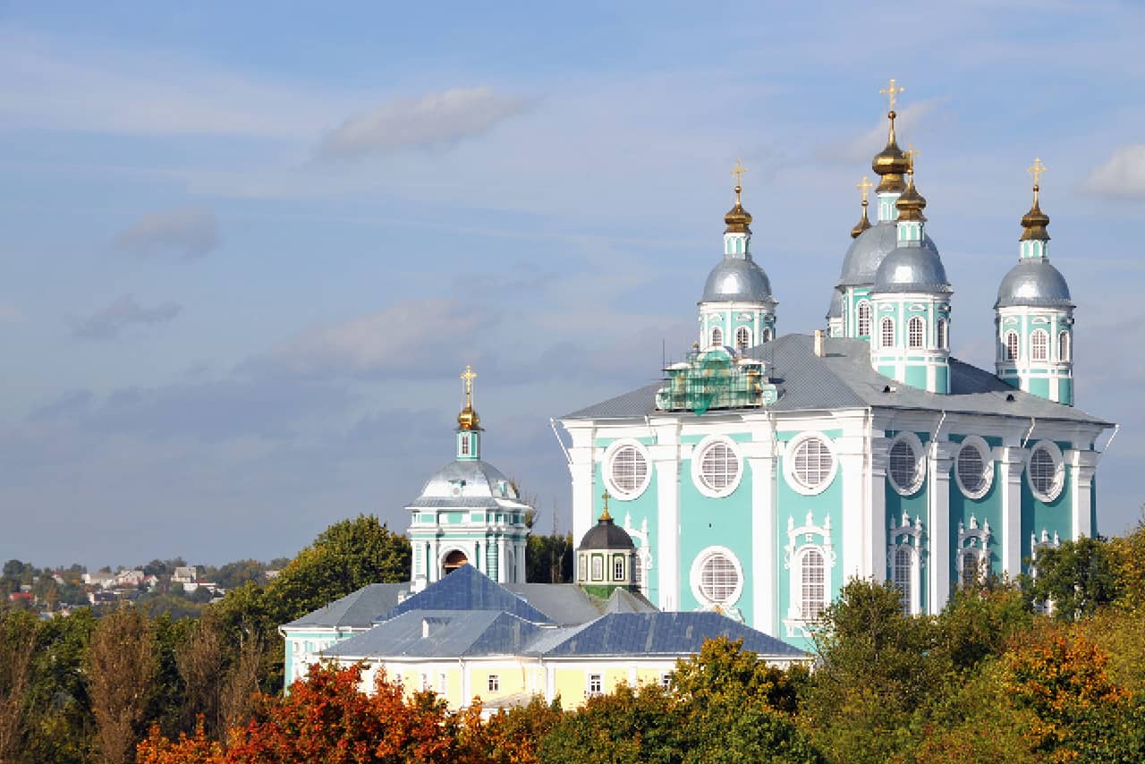 A giant turquoise and white cathedral in Ukrainian baroque style with two rows of round windows, silver domes with gilded tops