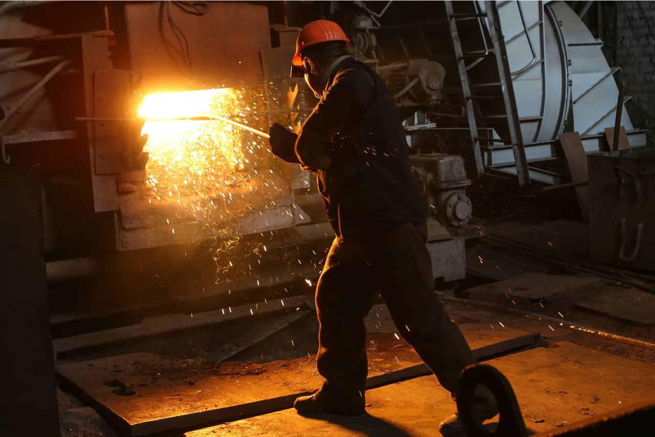 A worker wearing an uniform and helmet welds steel at a factory