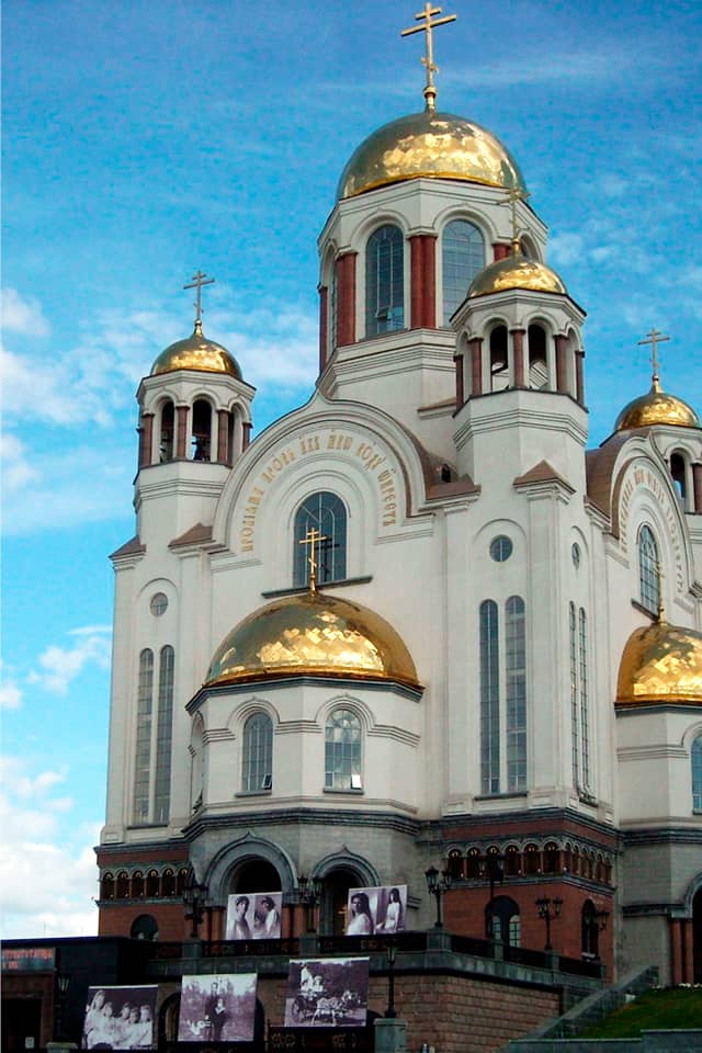 A recently build white orthodox church with red brick base, central dome with large arched windows and columns and four smaller domes around, gilded domes of a cathedral. Black and white photos in front of the cathedral