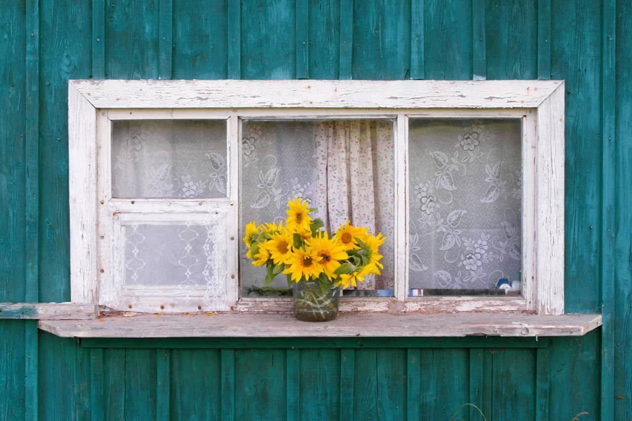 A bouquet of sunflowers in a vase on the window of a wooden house