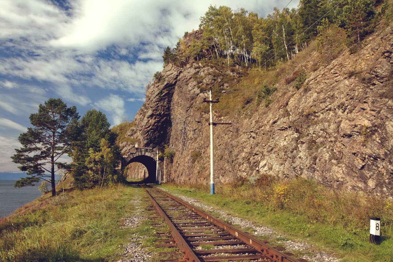 A railway track along the lake among rocks, railway tunnel