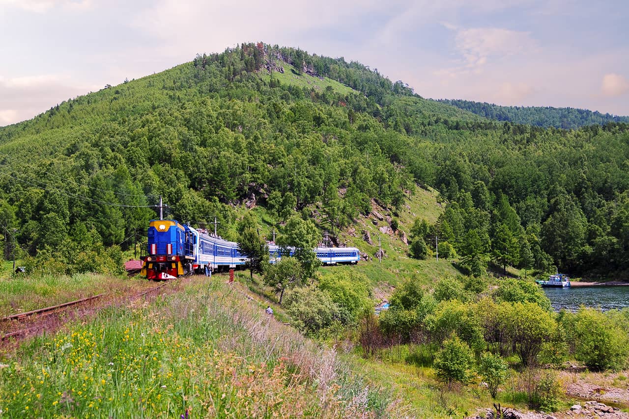 A Russian train on the railway track along the lake and pine forests