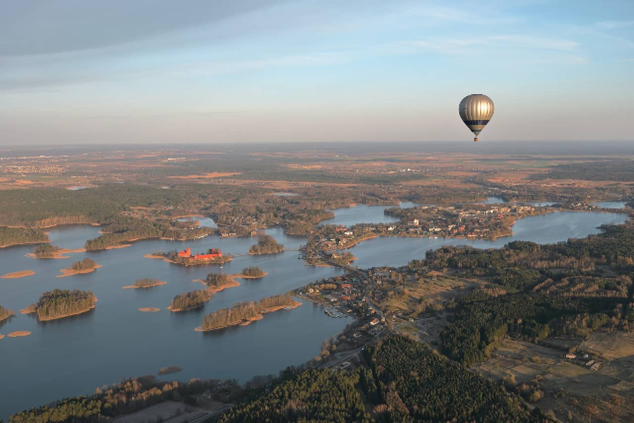 A hot air balloon flying over green forests and lakes, European countryside