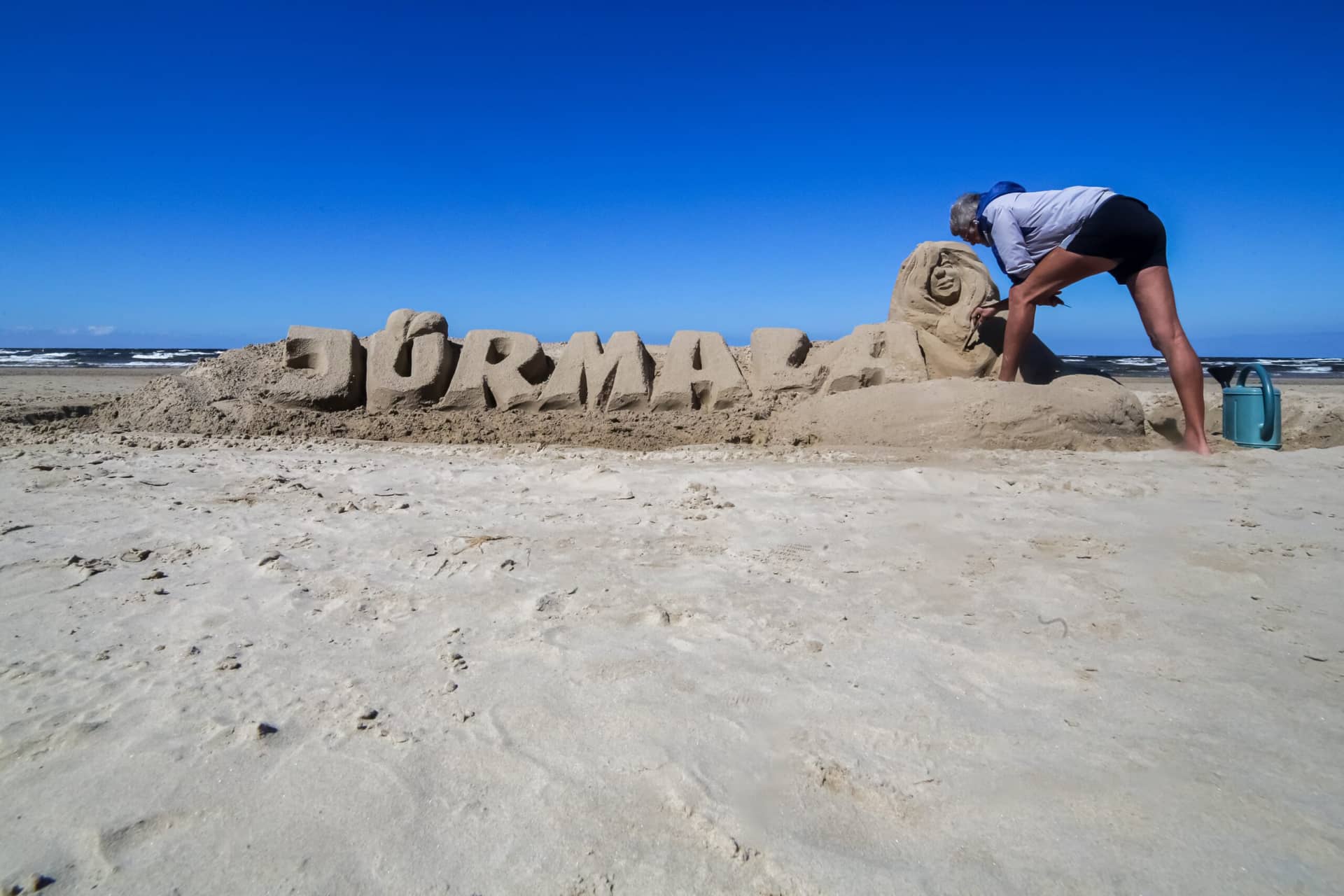 A person making sculpture of sand, sign Jurmala made of sand
