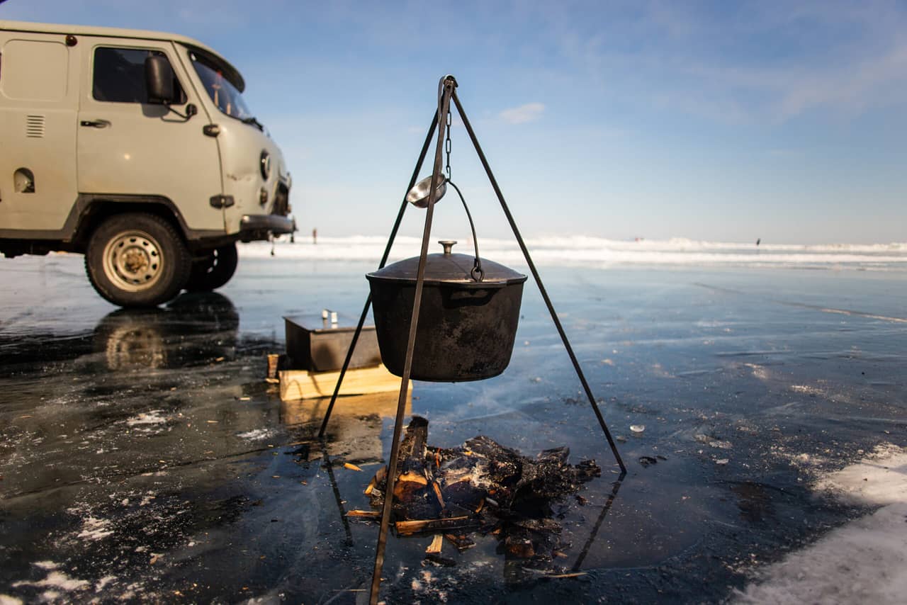 A cooking pot on open fire, a bonfire on the iced surface, a Russian off-road minibus