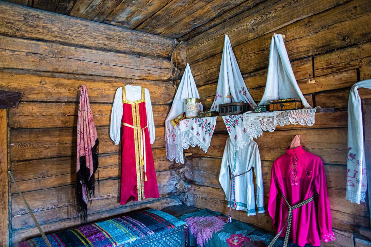 Interior of an old Russian wooden house, traditional Russian clothes hanged on the wall, boxes on a shelf decorated with white tissues