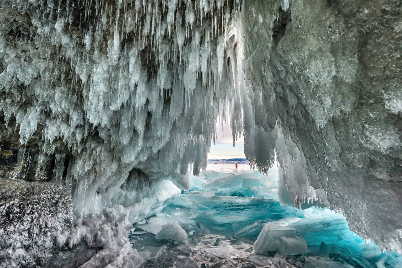 A view from inside of an ice cave covered with icicles, frozen lake in winter