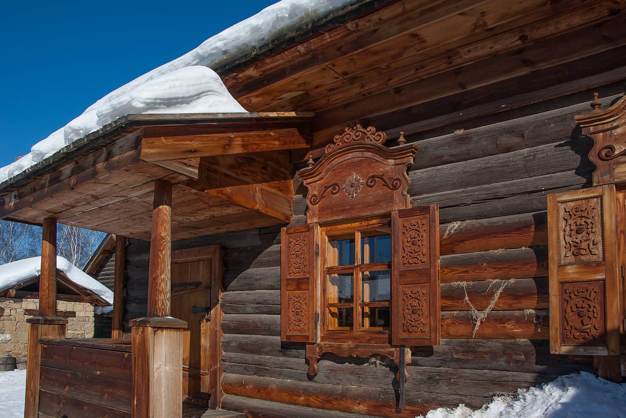 Russian wooden house with storm shutters in winter, snow on the roof of a wooden house.