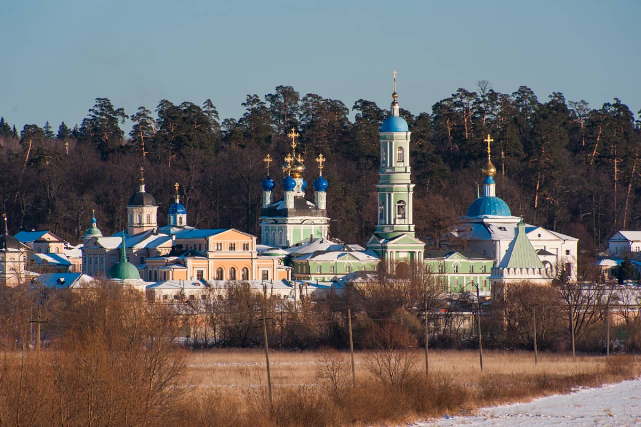 An architectural ensemble of an Eastern Orthodox Monastery, Green cathedral and bell tower with round blue dome, yellow building and other domes of orthodox churches around