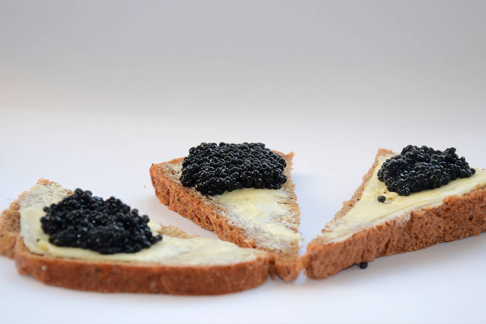 Three triangular pieces of bread with butter and black caviar