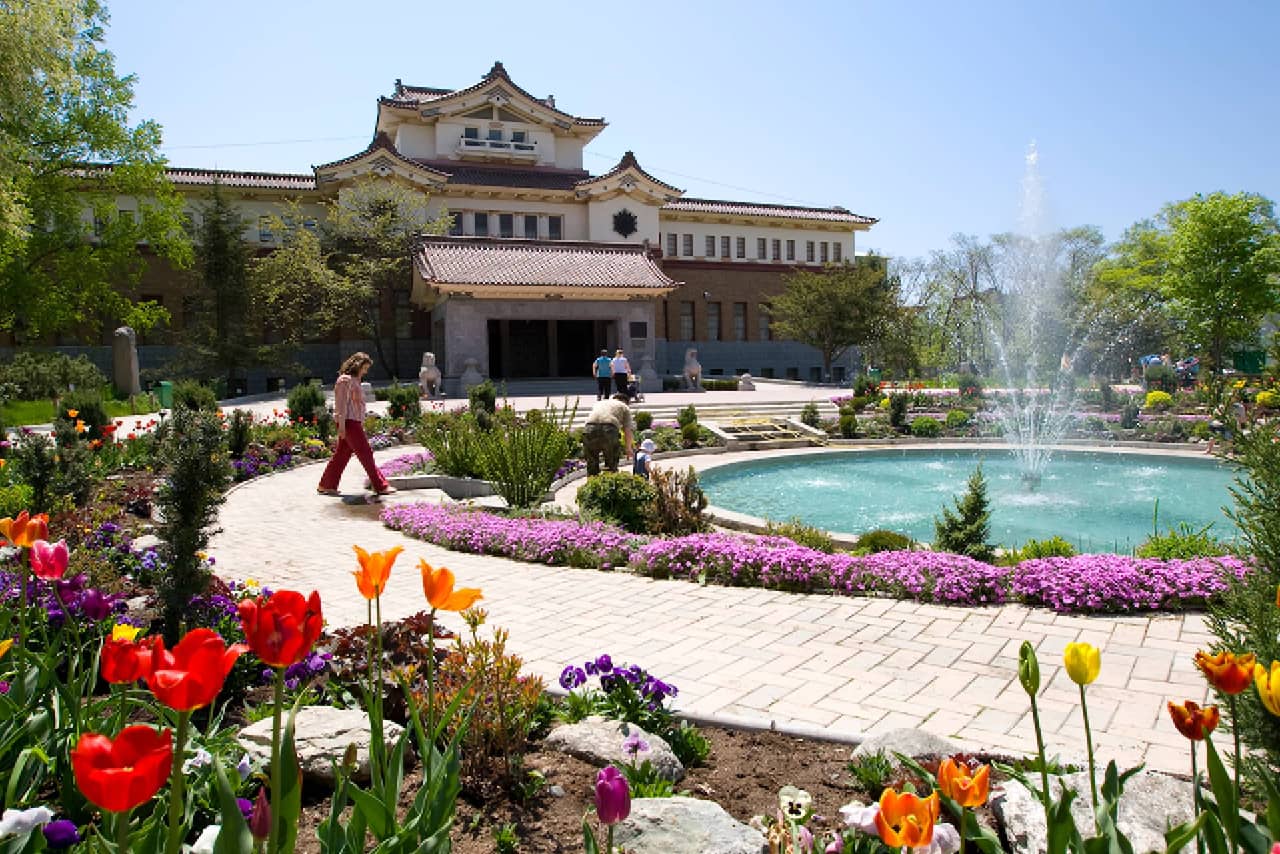 A museum in Russia in a building constructed in traditional Japanese style of "teican-dzukkuri" (imperial crown). A fountain and flowers in front of a building in Japanese style