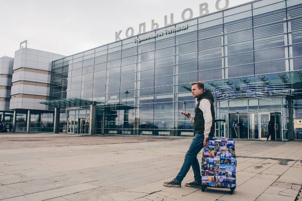A man sitting on his suitcase in front of an airport, a modern glass building of an airport in Russia